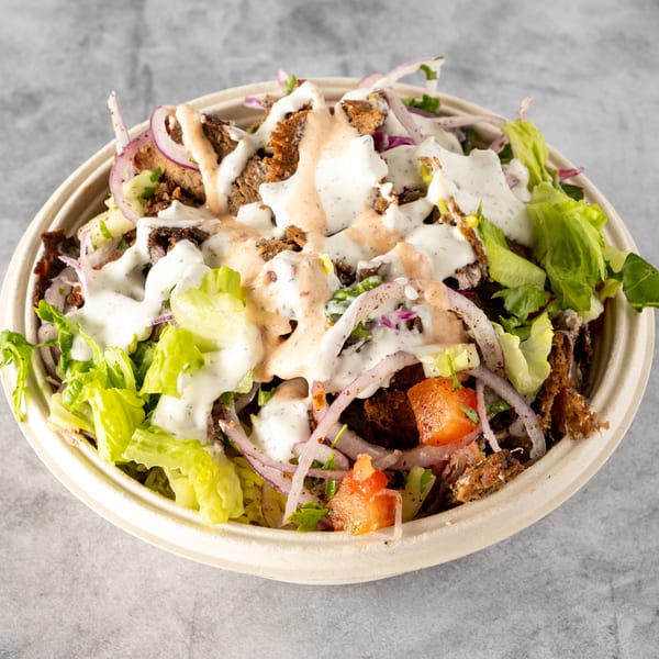 Gyro salad with meat, lettuce, tomatoes, red onions, and two sauces in a bowl.