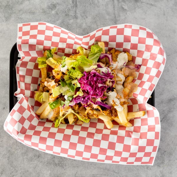 Loaded fries with chicken, lettuce, red cabbage, and two sauces in a red and white checkered paper.