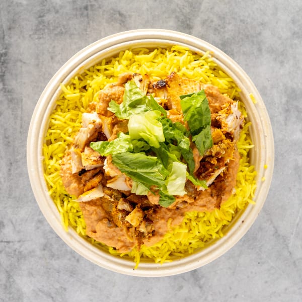 Overhead view of a chicken and rice bowl with yellow rice, chicken, sauce, and lettuce.