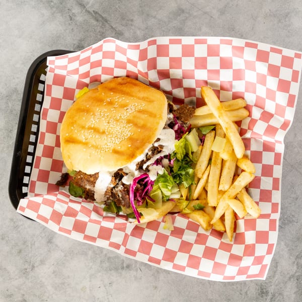 Doner kebab burger with white sauce, lettuce, red cabbage, and a side of fries in a basket.