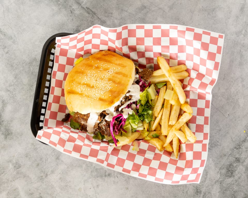 Doner kebab burger with white sauce, lettuce, red cabbage, and a side of fries in a basket.