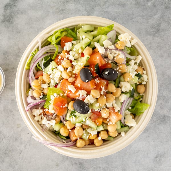 Overhead view of a colorful salad with chickpeas, olives, feta, and dressing on the side.