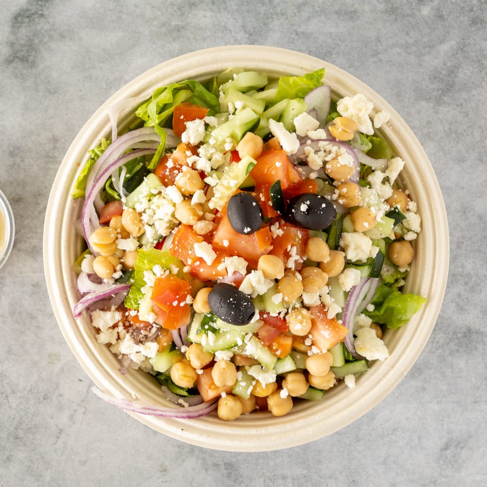 Overhead view of a colorful salad with chickpeas, olives, feta, and dressing on the side.